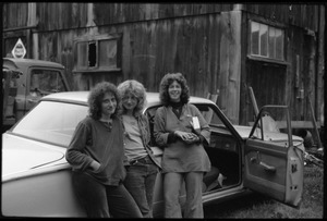 Janice Frey (center) and two friends standing by a car with open door in front of the barn, Montague Farm commune