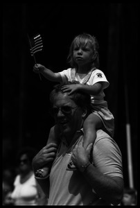 Girl waving a small American flag, sitting on her father's shoulders watching the Chesterfield's Fourth of July parade