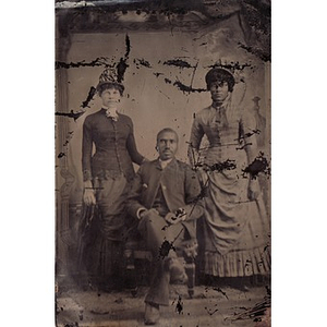 Two African American women standing next to a seated African American man