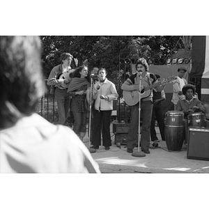 Musical group consisting of two men playing guitars, two women singing, and a young man playing drums, performs at a Latino street festival