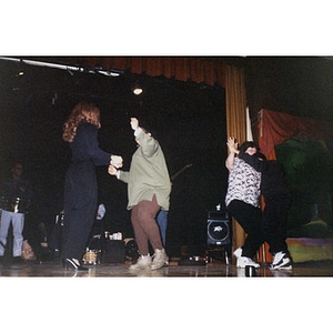 Women dancing on stage to music provided by the band behind them.