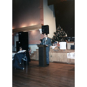 A man in a suit at the podium during a community Christmas celebration at the Jorge Hernandez Cultural Center.