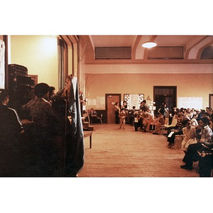 Audience of children and adults seated in a school auditorium.