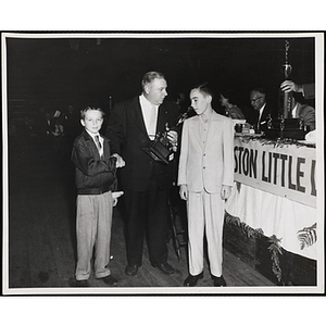 A man presents a South Boston Little League Baseball trophy to two boys and shakes hands with one of them