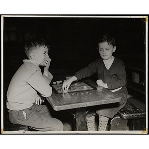 Two boys play checkers at a bench