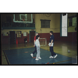 A woman, man, and girl talk in a gymnasium