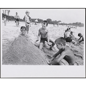 Three boys build a sand mound on a beach