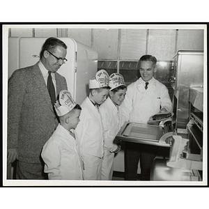 Three members of the Tom Pappas Chefs' Club pose with two men at a stove in a kitchen