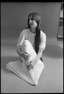 Studio portrait of a model in a loose-fitting shift, seated on the floor, looking up