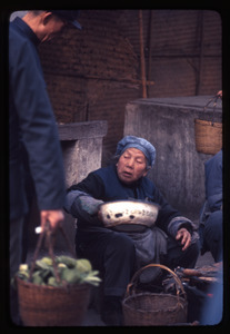 Old woman selling fish to man with basket of vegetables