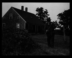 Old man, hoeing outside a Cape-style house