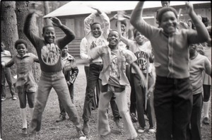 Inner City Round Table of Youth campers: group of African American children at summer camp, posed by camp building, raising hands and jumping