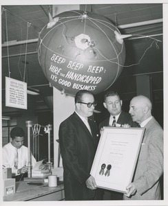 Two men stand with Willis C. Gorthy holding the 1957 Thumbs Up Award