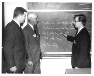 Trustee John P. Chase and two men have a discussion in front of a chalkboard at a Suffolk University Advisory Council meeting