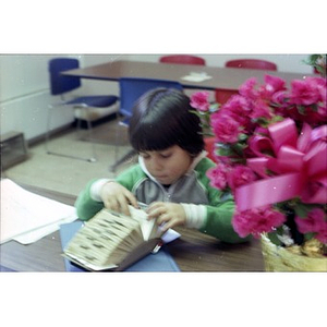 Hispanic boy seated at table looking at names and addresses in a Rolodex file at La Alianza Hispana, Boston