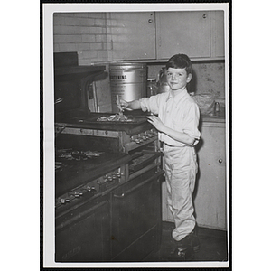A boy poses with a sheet pan and fork next to a stove in a kitchen