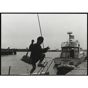 A girl steps from a sailboat to a dock in Boston Harbor