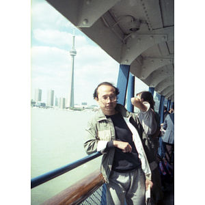 Chinese Progressive Association member leans against the railing on a ferry deck, with the Toronto skyline behind him