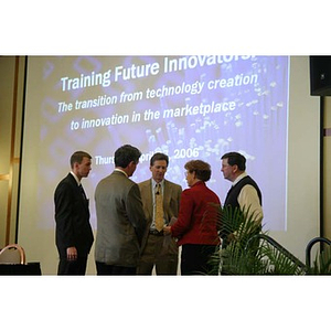 Five people stand in front of a projector screen at the Training Future Innovators Entrepreneurs Panel