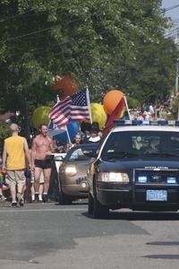 Police escort leading the approaching parade, with man dressed in Puritan costume walking behind : Provincetown Carnival parade