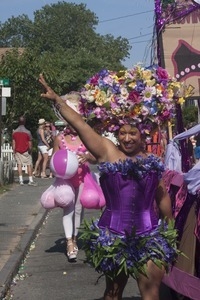 Marcher with large floral headress along side the parade float for Priscilla, Queen of the Cape : Provincetown Carnival parade