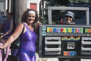 Woman in purple spandex standing next to a person decked out in a boombox radio costume: Provincetown Carnival parade
