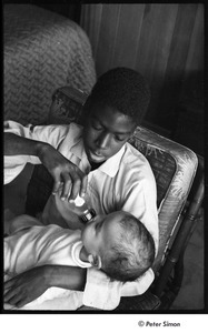 Party at Jackie Robinson's house: Rachel Robinson showing David Robinson  how to feed a baby with