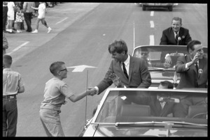 Young boy rushes up to shake hands with Robert F. Kennedy, riding in an open car at the Turkey Day parade while stumping for Democratic candidates in the northern Midwest