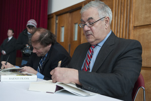 Author Stuart Weisman and Congressman Barney Frank (l. to r.) seated at a table in the Student Union Ballroom stage, UMass Amherst, signing copies of his biography
