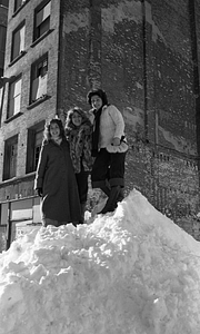 Three women posing atop large snowpile