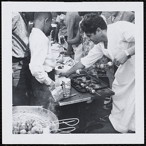 A man serves shesh kebabs to boys at a picnic