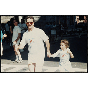 A man and a girl cross the finish line holding hands during the Battle of Bunker Hill Road Race