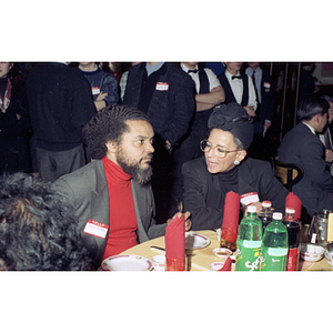 Rep. Byron Rushing chats with a woman at a restaurant table during Chinese Progressive Association's celebration of the Chinese New Year