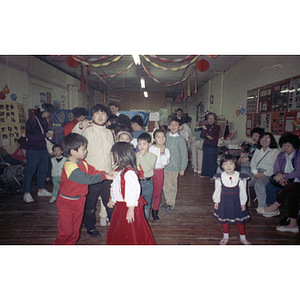 Adults observe a queue of children waiting for their turns at a piñata