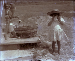Child drinking from a cup by a water pump, Mashpee, Mass.