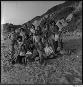Ram Dass and Satsang: Ram Dass posing on the beach with a group including Mirabai Bush and Chaitanya Maha Prabu to the left, Daniel Goleman behind them at left, Ronni Simon and Peter Simon at right with Cosmos the dog, and Tukaram Das at far back