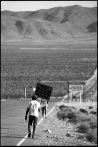 Activist on the road near the entrance to the Nevada Test Site holding a sign reading 'Stop nuclear weapons testing': Nevada Test Site peace encampment