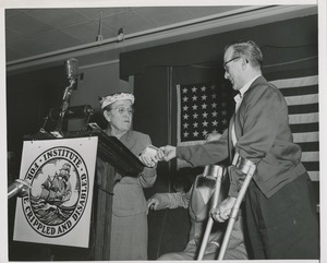 Unidentified man in forearm crutches handing a gift to a woman speaking at an ICD event