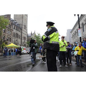A cameraman films video of the "One Run" race outside the Boston Public Library while a Boston Police officer looks on