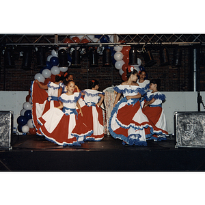 Several girls in Puerto Rican flag dresses dance on stage at the Festival Puertorriqueño