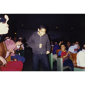 Boy walking down an aisle while the audience members in the auditorium applaud.