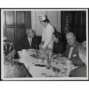 A member of the Tom Pappas Chefs' Club serves guests at a Bunker Hill dinner party with Executive Director of Boys' Club of Boston Arthur T. Burger seated at right