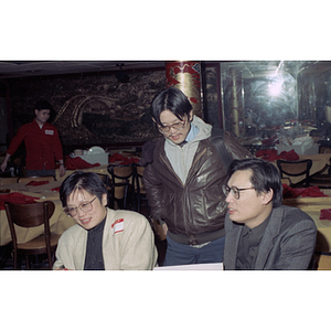 Two men and a woman sit at a table during a Chinese Progressive Association celebration of the Chinese New Year