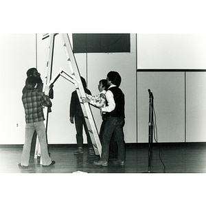 Five people move a ladder onstage in Josiah Quincy School auditorium in preparation for an event about the normalization of U.S. and China relations