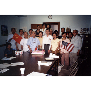 Chinese Progressive Association members gather around a man in blue who is cutting cake