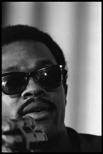 Bobby Seale: close-up portrait, speaking at a podium, wearing sunglasses