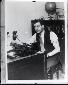 Mark Hellinger seated at his desk with a Remington typewriter