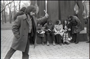 Interviewer with microphone standing in front of Richard Safft (reading) and other commune members during interview by Channel 5 news