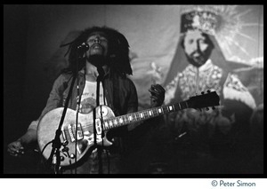 Bob Marley in concert, enrapt in the music while standing in front of a large banner with a portrait of Haile Selaisse