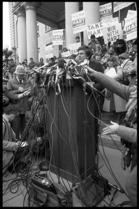 Gary Hart at a microphone-encrusted podium, addressing an crowd after renewing his bid for the Democratic nomination for the presidency